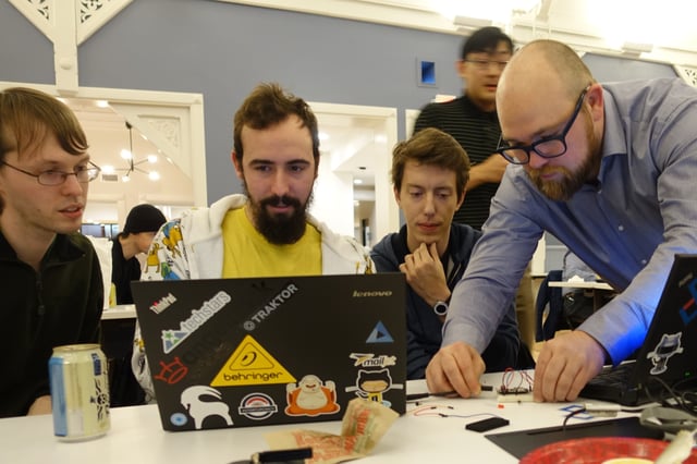A group of men behind a laptop with one person plugging in hardware to the laptop.