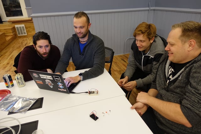 A group of four men around one laptop at Hack Night happy with what they are seeing.