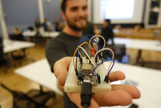 Man holding the Adafruit Feather Huzza with an internet button, LED, and temperature sensor.