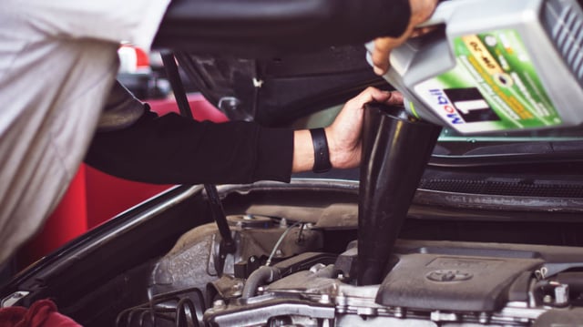 Mechanic filling a car with motor oil.