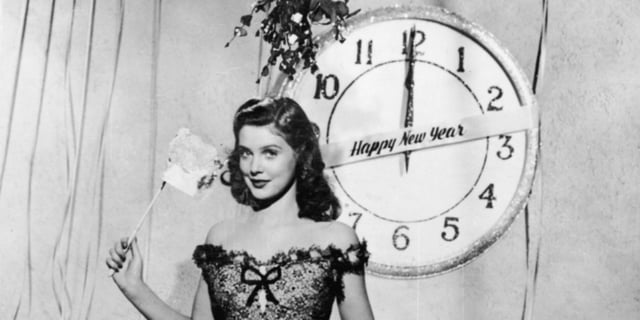 Pretty woman standing in front of a clock that says Happy New Year.