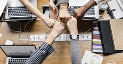 Team putting their fists together over a table of computers