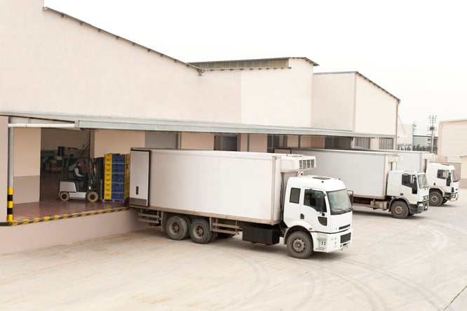 The back of a white warehouse with three large delivery trucks.