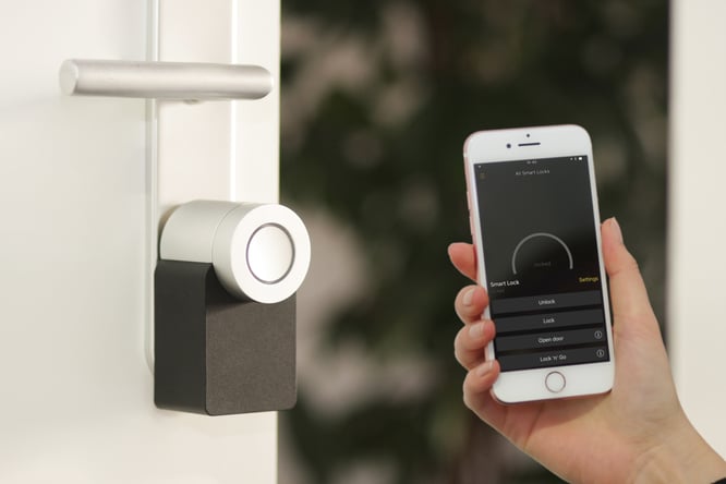 Iphone with a "Smart Locks" Application in a hand. Next to a Smart lock on a white door.