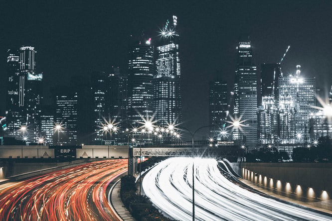 City skyline at night with a car headlight hyperlapse to indicate high speed.